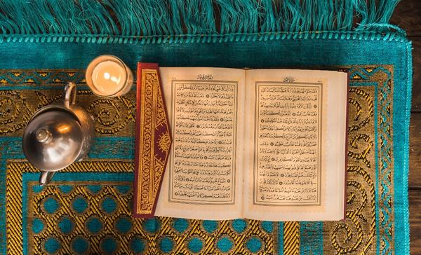 A Quran on a prayer mat with a candle