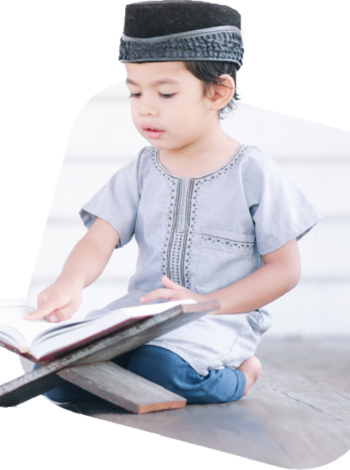 A young boy in traditional clothing reading the Quran.