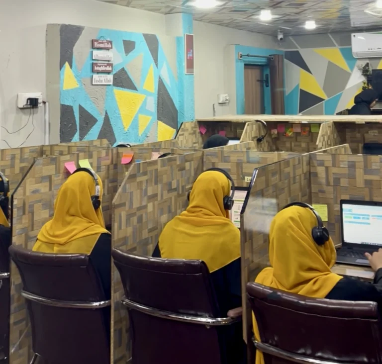 Female Quran teachers wearing yellow hijabs working on computers in an online Quran academy office