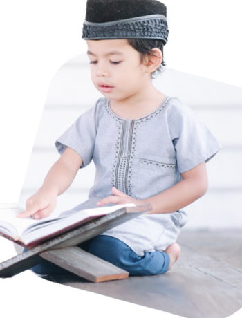 A young boy in traditional clothing reading the Quran.